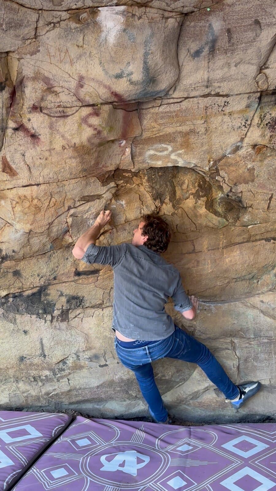 A climber pulling on a low sandstone overhang above crash pads