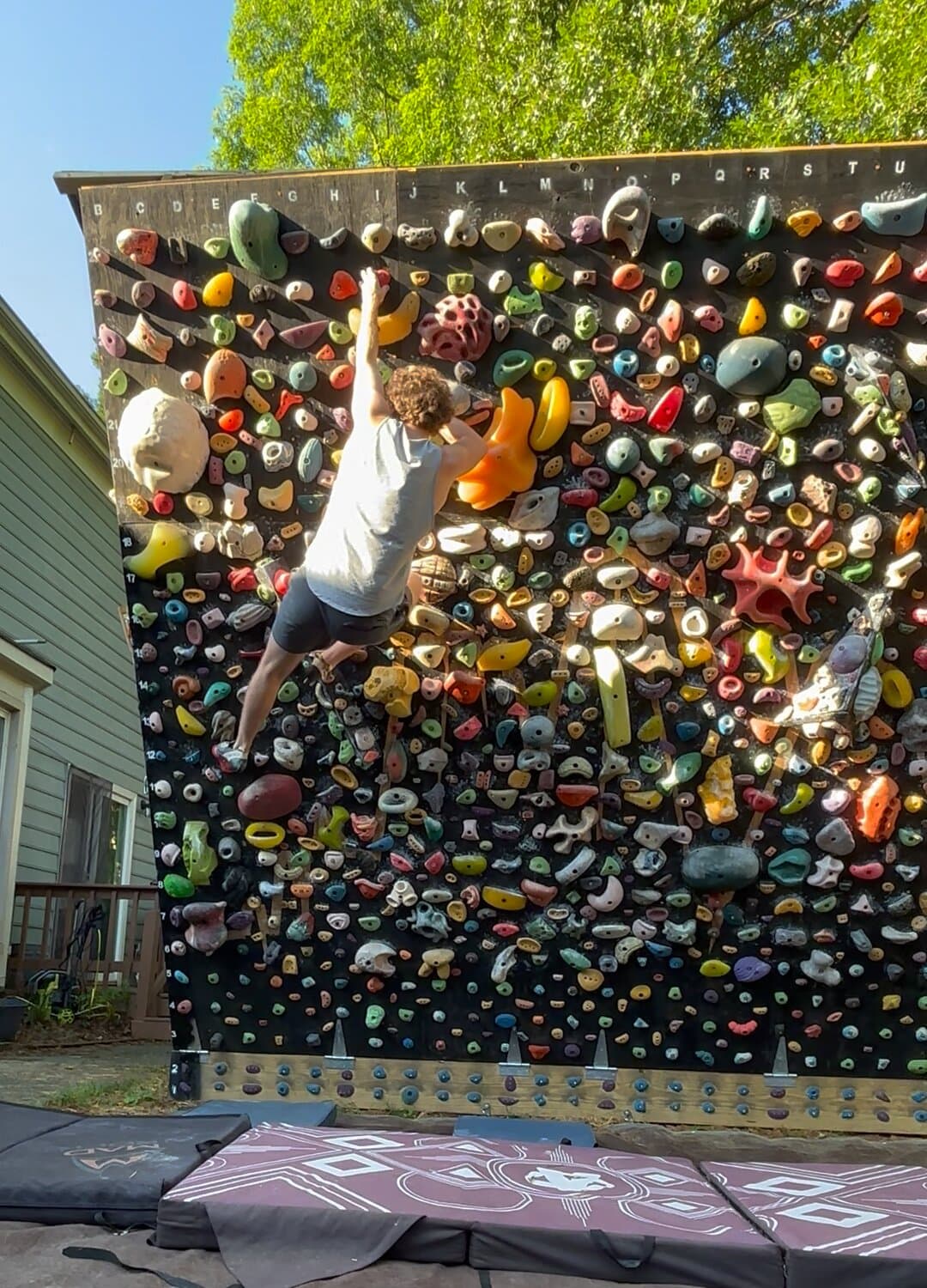 A climber in a white tank top high on the backyard wall