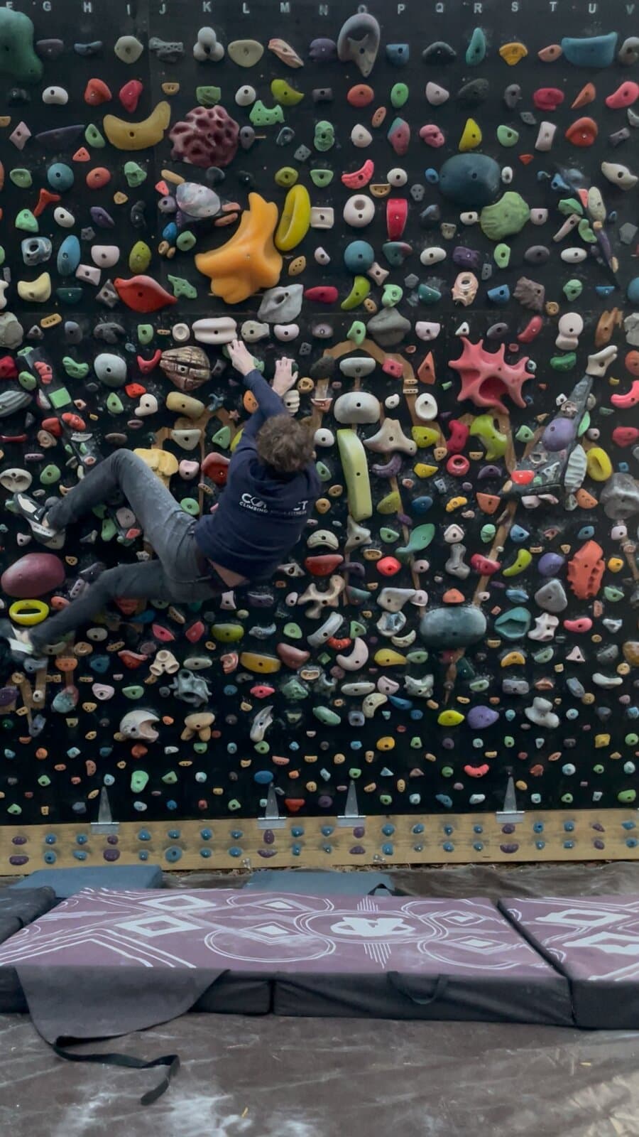 A climber in a navy sweatshirt mid-move on the backyard wall