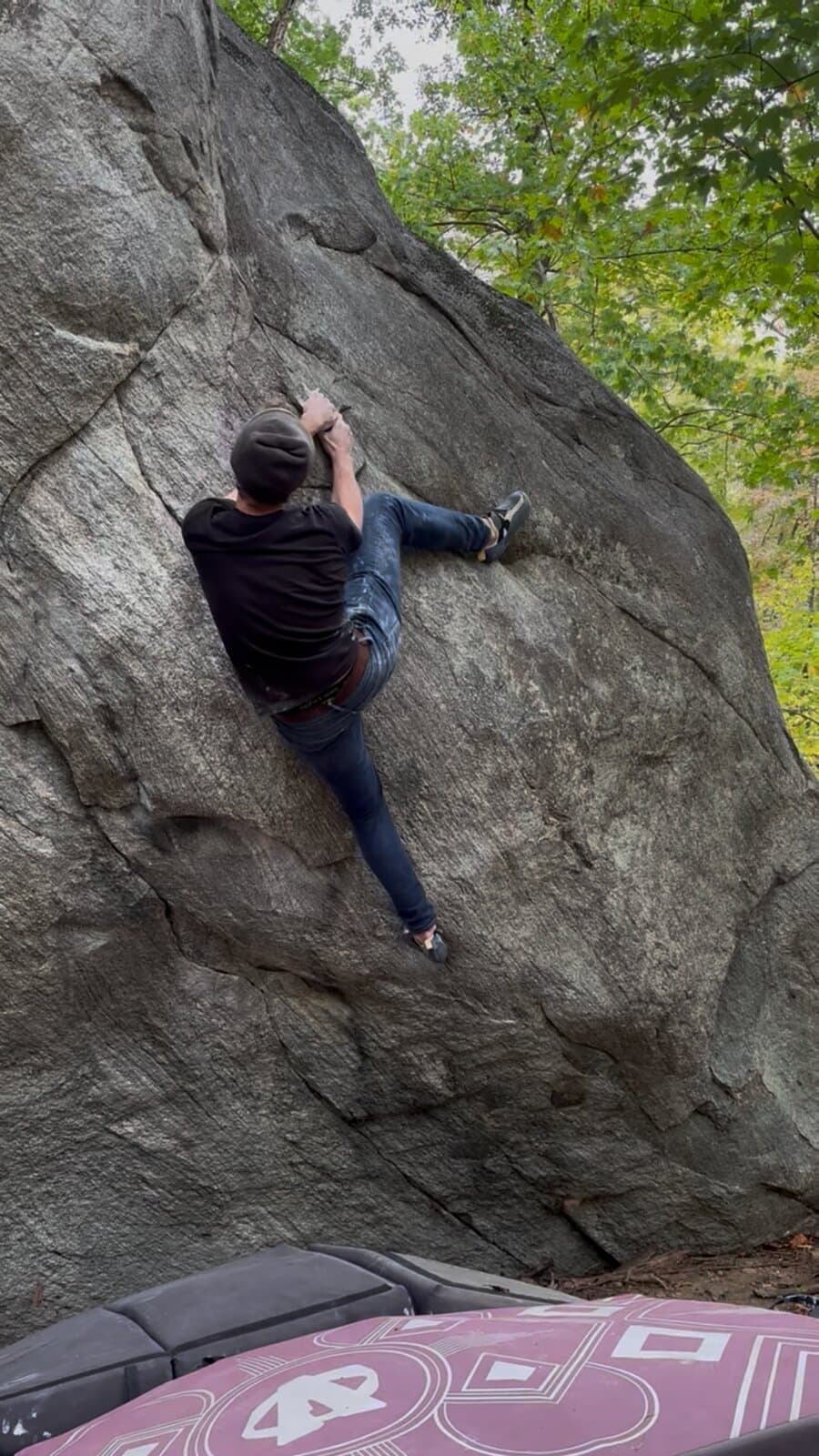 A climber in a beanie on a steep gray boulder
