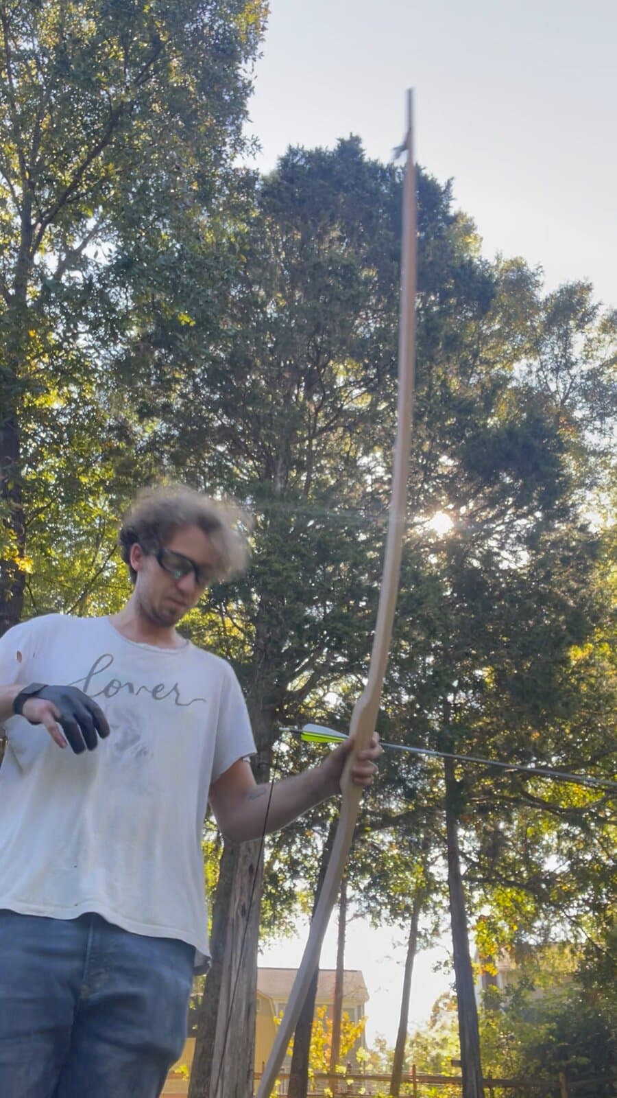 A tall wooden longbow held upright at full length, trees behind