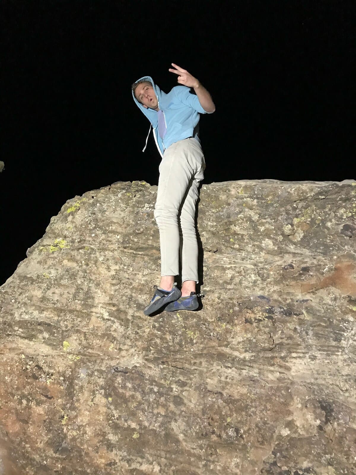 A climber in a light blue hoodie standing on top of a sandstone boulder at night