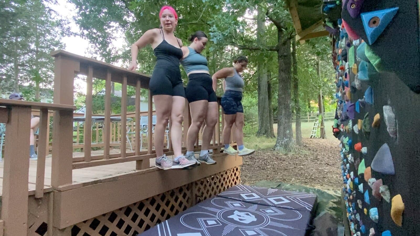 Three contestants standing on the outside edge of a deck railing